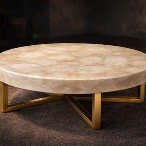 May include: A circular coffee table featuring a light beige stone top and gold-coloured metal legs. The table has a contemporary design and is placed on a dark brown rug. The table's top displays a unique, natural pattern.