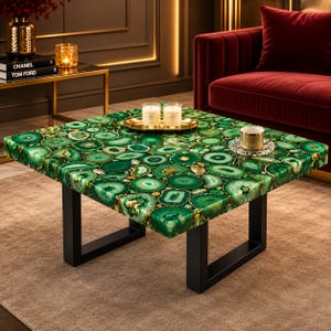 May include: A square coffee table featuring a tabletop composed of numerous polished green agate slices with gold-toned edges. The table is supported by a sturdy black metal frame with four U-shaped legs, providing a stable base for the stone surface.