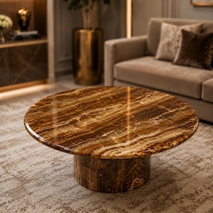 Op de afbeelding: Een ronde salontafel met een gepolijst, bruin en tan marmeren blad. De tafel heeft een cilindrische voet en staat op een patroonkleed. Het ontwerp van de tafel is modern en elegant, geschikt voor een woonkamer.