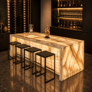 May include: A backlit white onyx bar with a warm glow, featuring a rectangular shape and a textured surface. Four black metal stools with woven seats are positioned in front. The bar has the text "WHITE ONYX BAR" on the side.