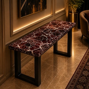 May include: A rectangular console table featuring a deep red, marble-patterned top with prominent white veining. The table is supported by two sturdy, black metal U-shaped legs that provide a stable base for the polished, glossy surface.