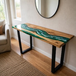 Puede incluir: Una consola de madera con diseño de río. La encimera presenta una veta de madera natural con un río de resina epoxi verde y blanco. La mesa tiene patas de metal negro, creando una estética moderna. Mide aproximadamente 150 cm de largo.