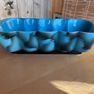 May include: A rectangular, turquoise ceramic planter with a scalloped rim. The planter features a dark blue base and decorative black accents. This vintage piece is suitable for indoor or outdoor use.