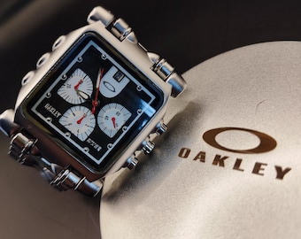 Cronógrafo Oakley Minute Machine Style: reloj cuadrado de acero plateado con esfera negra y diseño industrial Y2K.