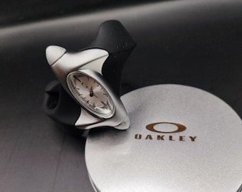 Reloj Oakley estilo torpedo: esfera plateada, diseño minimalista futurista estilo Y2K con correa negra.