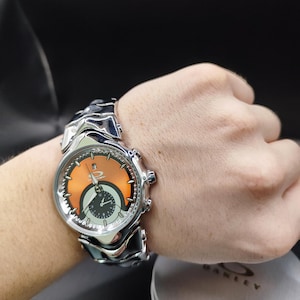Pu&ograve; includere: Un orologio da polso argentato con quadrante arancione e nero &egrave; mostrato su un polso. L'orologio ha un cinturino unico e strutturato e diversi quadranti. Il quadrante dell'orologio presenta il logo del marchio. L'orologio &egrave; un accessorio elegante.