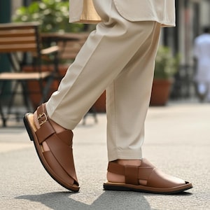 May include: Brown leather sandals with a strap and buckle closure. The sandals have a flat sole and are worn with beige pants. The sandals are designed with a crisscross strap design over the foot.
