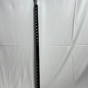 May include: A black walking cane with a curved handle and a silver metal collar. The shaft is black with a series of decorative cutouts. The cane is designed for support and mobility.
