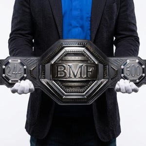 Può includere: Una cintura da campionato nera con una grande placca metallica centrale che riporta il testo BMF, BADDEST e MOTHERFUCKER. Le placche laterali mostrano i numeri 244 e 500, insieme al testo NOV 2, 2014, NOV 2, 2019 e MSG NYC in finitura metallica.