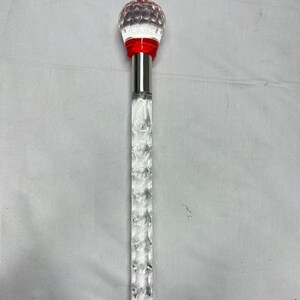 May include: A clear, decorative cane with a faceted, crystal-like shaft and a round, textured top. The top is clear with red accents and a silver metal collar. The cane is designed for decorative purposes.