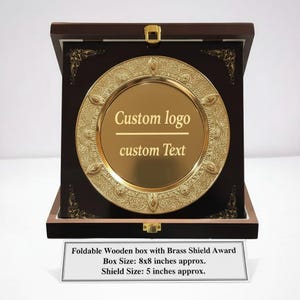 May include: A wooden box with a brass shield award. The box is dark brown with a gold clasp. The shield is gold with the text "Custom logo" and "custom Text". The box is approximately 8x8 inches.