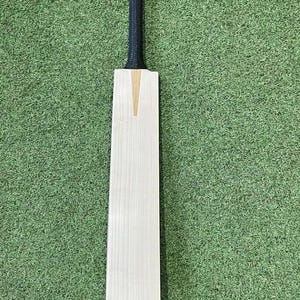 May include: A cricket bat with a light wood blade and a black grip. The blade has a light brown accent in the center. The bat is set against a green background.