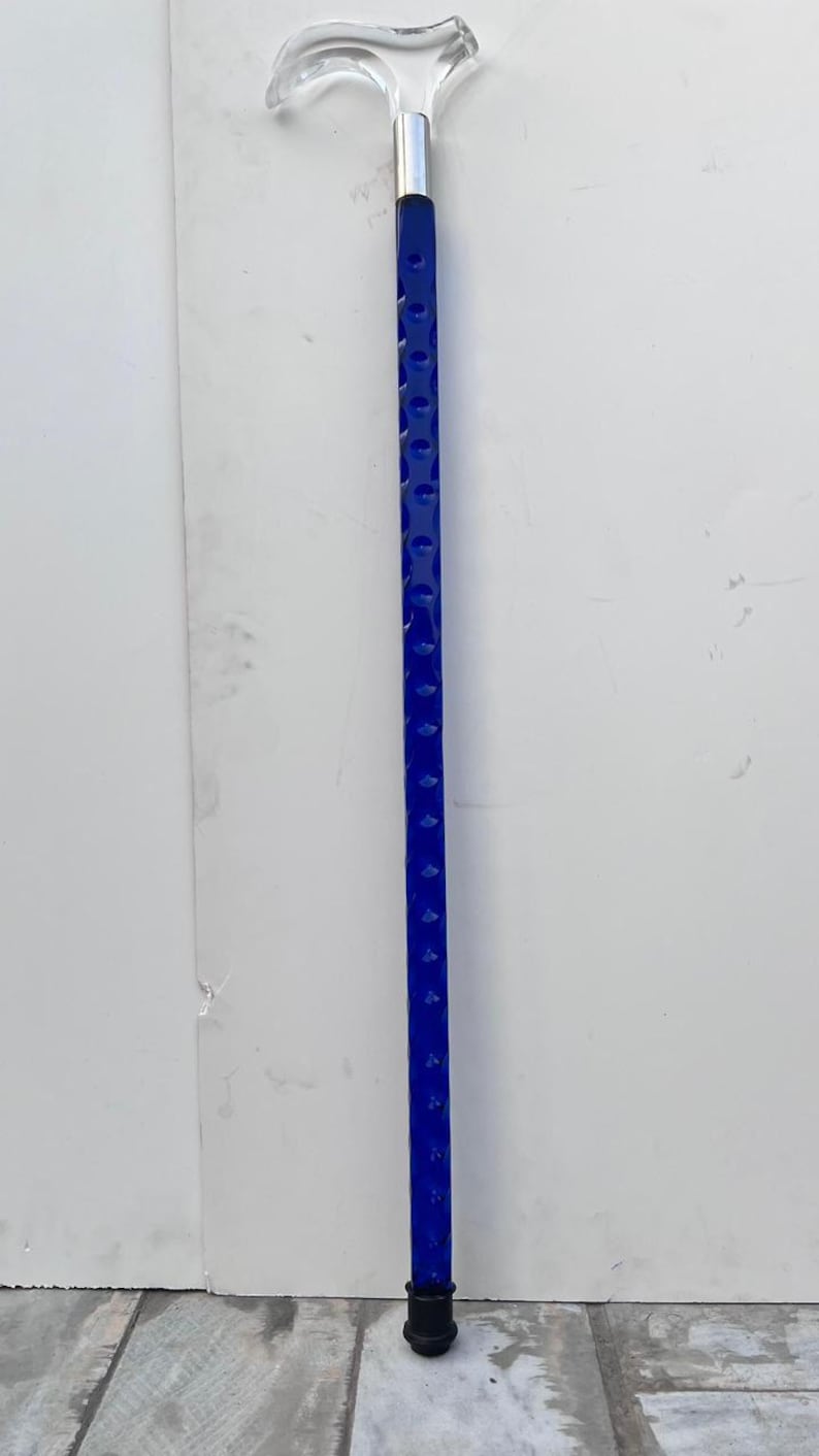 May include: A clear acrylic walking cane with a curved handle and a silver-colored metal collar. The shaft is a vibrant blue with a series of evenly spaced, circular indentations. The cane's tip is black.
