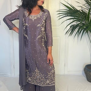 May include: A dark grey long-sleeved tunic and wide-leg trousers set featuring intricate silver floral embroidery and scattered pearl-like embellishments. The ensemble includes a matching sheer grey dupatta draped over one shoulder.