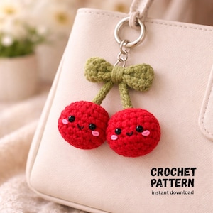 May include: A handmade crochet cherry keychain with a smiling face, attached to a silver keyring. The cherries are red with green stems and a green bow. The text "CROCHET PATTERN" is visible.