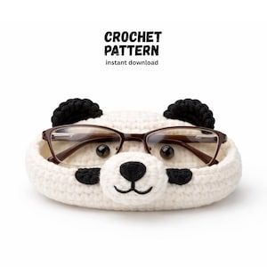 Könnte beinhalten: Ein weißer, gehäkelter Brillenhalter in Pandaform mit schwarzen Akzenten, der eine Brille mit braunem Rahmen hält. Der Halter hat schwarze Ohren und eine schwarze Nase und Mund. Der Text oben lautet "CROCHET PATTERN instant download."