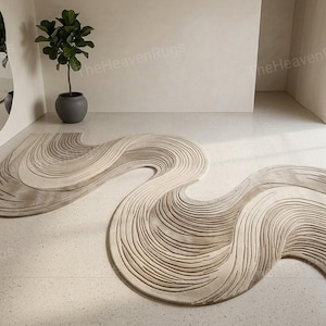 May include: Two beige and brown abstract rugs with a wavy design are displayed on a light-colored floor. A large, irregularly shaped mirror hangs on the wall, reflecting the rugs. A potted plant sits nearby, and a large window is visible.