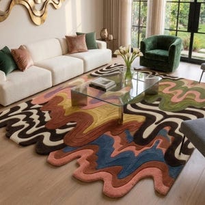 May include: A large area rug featuring an irregular, wavy, organic shape with a multi-colored pattern of flowing lines in shades of pink, blue, brown, yellow, and cream. The rug has a textured, tufted surface and covers a portion of the floor.