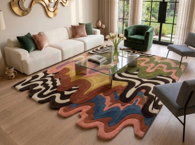 May include: A large area rug featuring an irregular, wavy, organic shape with a multi-colored pattern of flowing lines in shades of pink, blue, brown, yellow, and cream. The rug has a textured, tufted surface and covers a portion of the floor.