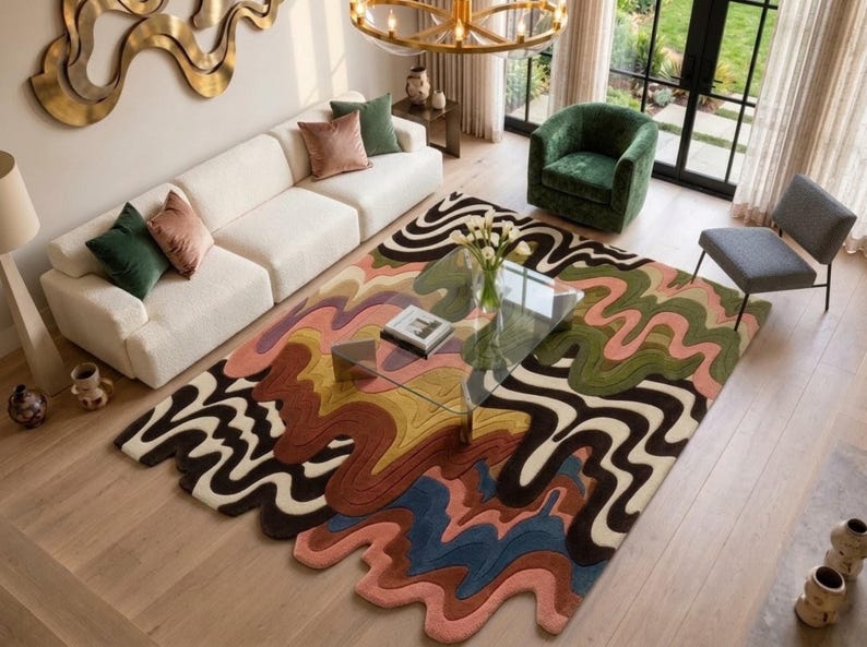 An irregular shaped hand-tufted wool area rug featuring abstract wavy lines and a retro topographical color palette of mustard, rust, olive green, blush, slate, and chocolate brown, styled under a glass coffee table in a modern living room.