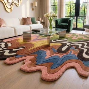May include: A large area rug featuring a multi-colored, wavy, liquid-like pattern with irregular, flowing edges. The design incorporates shades of pink, blue, brown, yellow, green, and cream in a thick, textured pile that covers the floor.