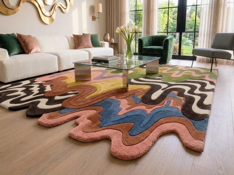 May include: A large area rug featuring a multi-colored, wavy, liquid-like pattern with irregular, flowing edges. The design incorporates shades of pink, blue, brown, yellow, green, and cream in a thick, textured pile that covers the floor.