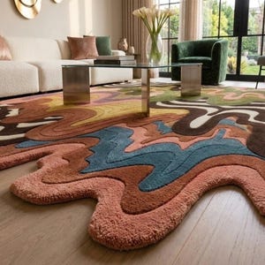May include: A large area rug featuring an irregular, organic shape with a multi-colored, wavy, and layered pattern. The design incorporates shades of terracotta, dusty pink, deep blue, olive green, dark brown, and cream in a fluid, abstract style.