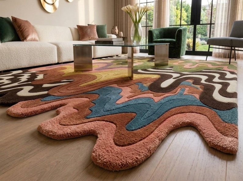 May include: A large area rug featuring an irregular, organic shape with a multi-colored, wavy, and layered pattern. The design incorporates shades of terracotta, dusty pink, deep blue, olive green, dark brown, and cream in a fluid, abstract style.