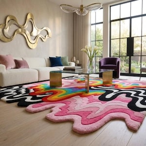 May include: A large, irregularly shaped area rug featuring a vibrant, multi-colored design with wavy, liquid-like patterns in shades of pink, black, white, yellow, orange, green, and blue, covering a light-colored wooden floor in a living room.