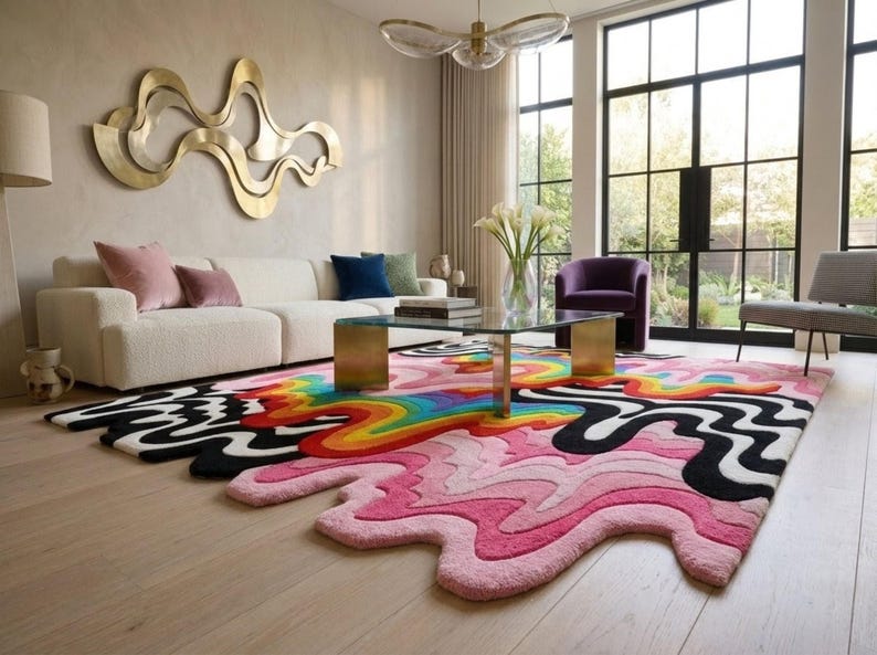 May include: A large, irregularly shaped area rug featuring a vibrant, multi-colored design with wavy, liquid-like patterns in shades of pink, black, white, yellow, orange, green, and blue, covering a light-colored wooden floor in a living room.
