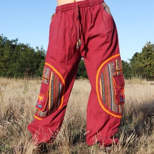 Peut inclure: Pantalon bordeaux avec des patchs et des poches décoratives. Les patchs présentent des motifs géométriques colorés et des broderies. Le pantalon a une taille à cordon et est fait d'un tissu léger, adapté aux tenues décontractées.