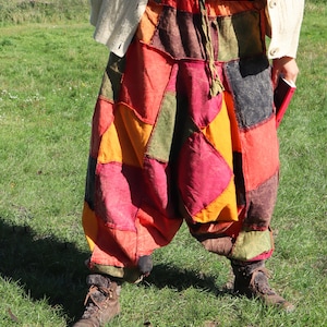 Op de afbeelding: Patchwork harembroek in tinten rood, oranje, groen en bruin. De broek heeft een trekkoord in de taille en wordt gedragen met bruine laarzen. Het patchwork ontwerp is gemaakt van verschillende stoffen die aan elkaar zijn genaaid.