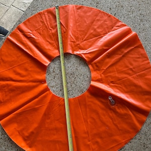 May include: A bright orange circular inflatable ring with a central opening. A yellow measuring tape is placed vertically across the object, showing a diameter of approximately 48 inches from the outer edge to the opposite outer edge.