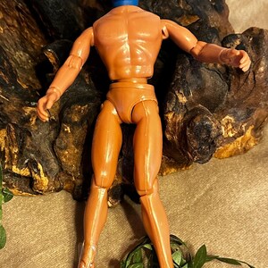 May include: A vintage action figure of a superhero, featuring a blue mask with a white "A" on a black background. The figure is tan with articulated joints and stands in a dynamic pose. The figure is approximately 12 inches tall.