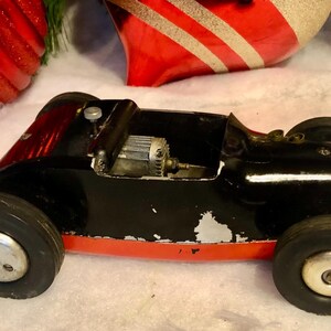 May include: A classic black toy racing car with red detailing and rubber tyres. The car features a silver engine and shows signs of wear. A vintage toy, possibly from the mid-20th century.