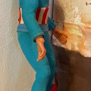 May include: A vintage action figure of a superhero, wearing a blue and red costume. The figure has a blue cowl, a black mask, and red boots. The figure's belt has a red and white striped design.