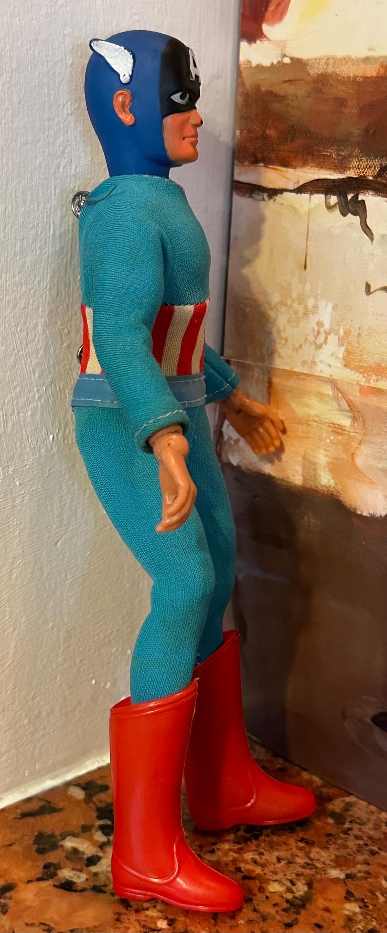 May include: A vintage action figure of a superhero, wearing a blue and red costume. The figure has a blue cowl, a black mask, and red boots. The figure's belt has a red and white striped design.