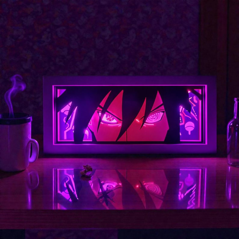 Pu&ograve; includere: Un'opera d'arte rettangolare e illuminata con gli occhi stilizzati di un personaggio anime in tonalit&agrave; rosse e rosa. L'opera &egrave; incorniciata da un bordo bianco ed emette una luce viola. Una tazza e una bottiglia sono visibili sul tavolo.