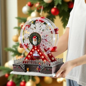Könnte beinhalten: Ein weihnachtliches Riesenrad-Dekorationsobjekt in Rot und Weiß. Das Rad hat ein Schneeflocken-Design und die Worte "Merry Christmas" um ein Santa Claus-Bild. Die Basis ist eine Ziegelstruktur mit Miniaturfiguren.
