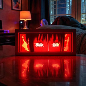 Pu&ograve; includere: Un'opera d'arte rettangolare illuminata in stile anime. L'opera presenta un paio di grandi occhi stilizzati con iridi bianche e pupille nere, su sfondo rosso. Il pezzo &egrave; in una cornice di legno, che proietta un bagliore rosso.