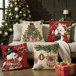 May include: Four Christmas-themed cushions with festive designs. One cushion features a Christmas tree, another Santa Claus, a snowman, and baubles. The cushions are on a neutral sofa with a Christmas tree in the background.
