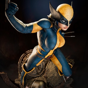 Puede incluir: Figura detallada de una superheroína en una pose dinámica, vestida con un traje azul y amarillo con una máscara. La figura tiene garras extendidas y está colocada sobre un fondo oscuro. La base presenta un emblema circular y un casco.