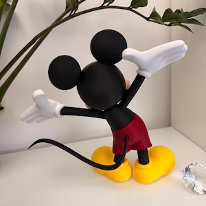 Puede incluir: Figura de Mickey Mouse negro con guantes blancos, pantalones cortos rojos y zapatos amarillos. La figura tiene una cola y orejas negras. La figura posa con los brazos extendidos. Un art&iacute;culo decorativo para los fan&aacute;ticos de Disney.
