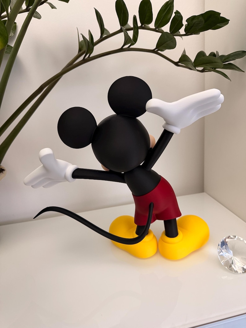 Puede incluir: Figura de Mickey Mouse negro con guantes blancos, pantalones cortos rojos y zapatos amarillos. La figura tiene una cola y orejas negras. La figura posa con los brazos extendidos. Un art&iacute;culo decorativo para los fan&aacute;ticos de Disney.