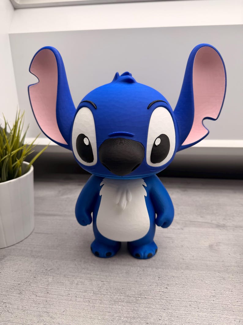 Peut inclure: Figurine bleue repr&eacute;sentant le personnage de Stitch, avec de grandes oreilles aux int&eacute;rieurs roses, de grands yeux et un nez noir. La figurine a un ventre blanc et se tient debout. Objet de collection.