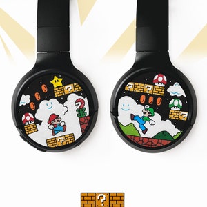 Picture of black headphones, hand-painted with a Super Mario 8 bit video game inspired design. Including the Mario brothers, Mario and Luigi, 1up mushrooms, Piranha plant, Question blocks, Starman and Brick Blocks on a black background.
