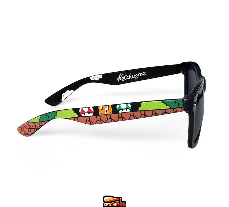 Picture of black sunglasses, hand-painted with a Super Mario 8 bit video game inspired design. Including 1up mushrooms, Piranha plant, Question blocks, Starman and Brick Blocks on a black background.