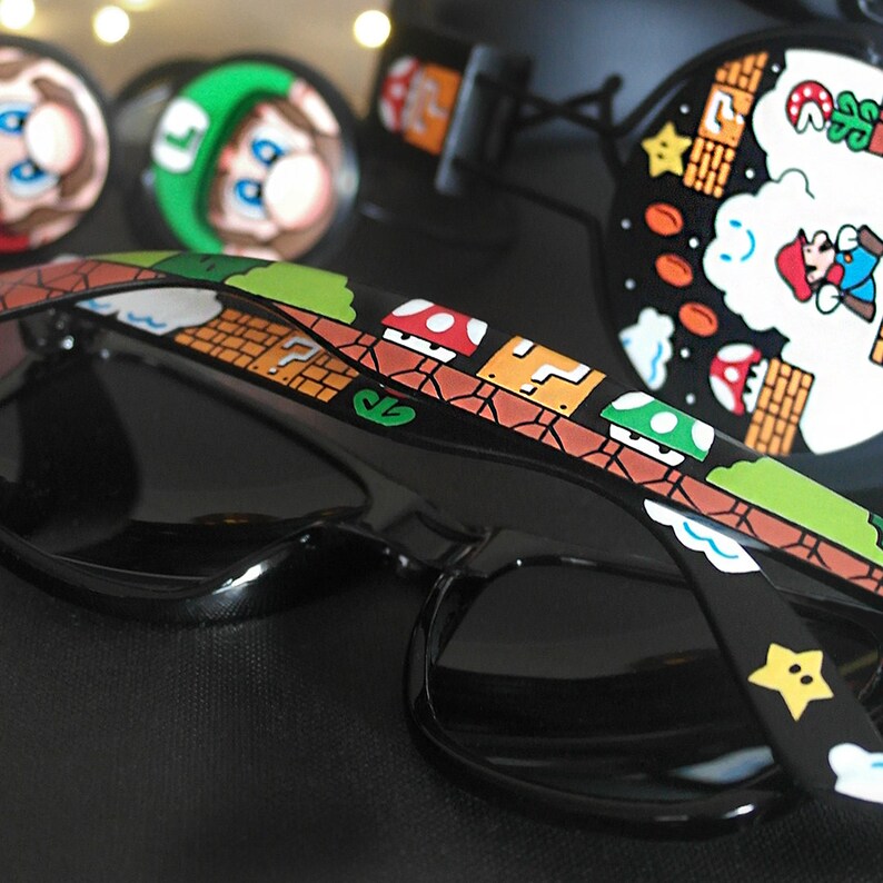 Picture of black sunglasses and headphones, painted with a Super Mario 8 bit video game inspired design. Including the Mario brothers, Mario and Luigi, 1up mushrooms, Piranha plant, Question blocks, Starman and Brick Blocks on a black background.