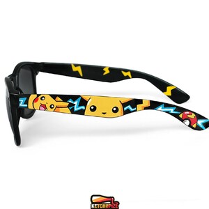 Picture of black sunglasses, hand-painted with a Pokemon design, including yellow Pikachu, blue and white bolts and red and white Pokeballs on a black background, in white, black, yellow, red and blue colors.