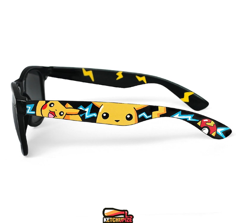 Picture of black sunglasses, hand-painted with a Pokemon design, including yellow Pikachu, blue and white bolts and red and white Pokeballs on a black background, in white, black, yellow, red and blue colors.